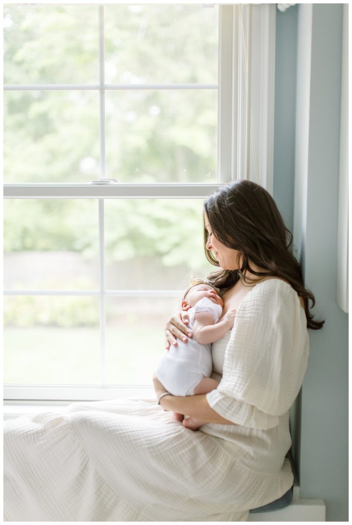 A mother snuggling her new baby at home sitting in a window seat
