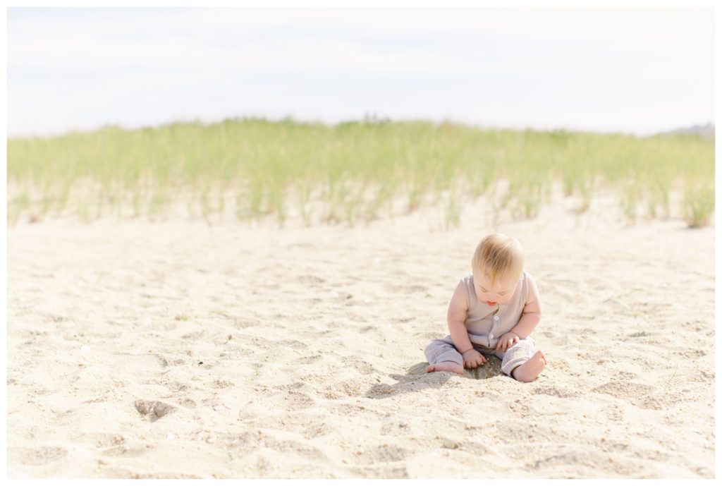 A little boy playing in the sand in front of some grassy dunes
