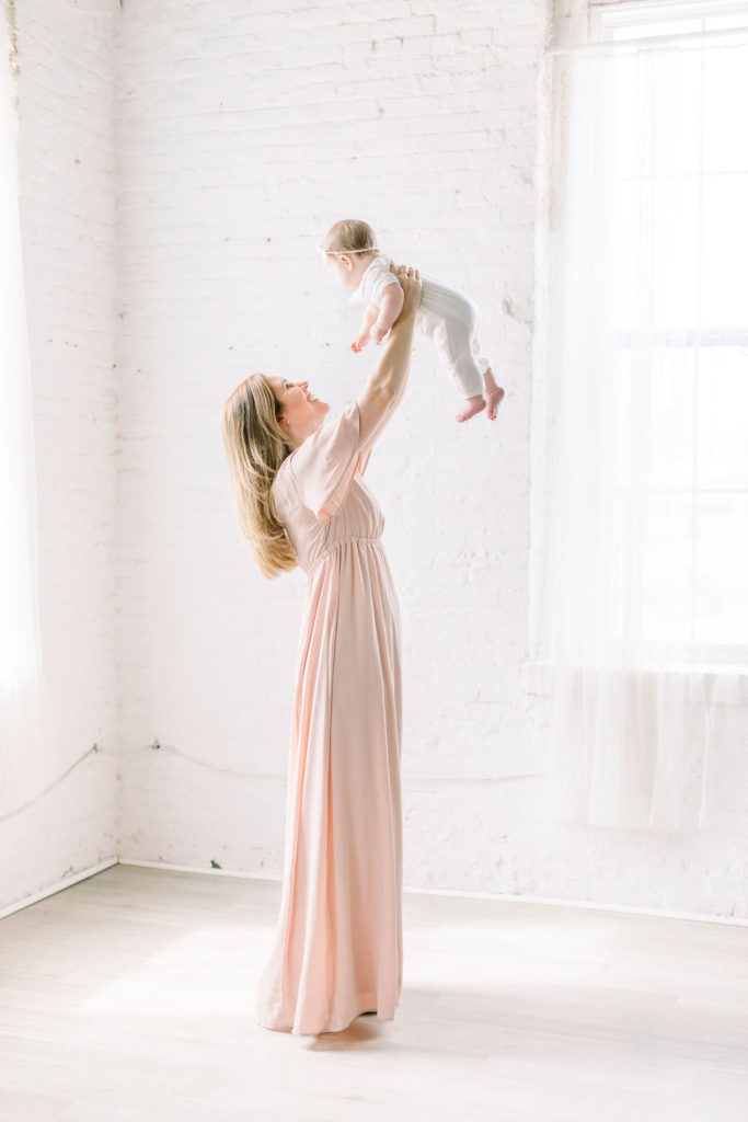 a mother wearing a pink dress and her daughter in a white romper during a studio motherhood session