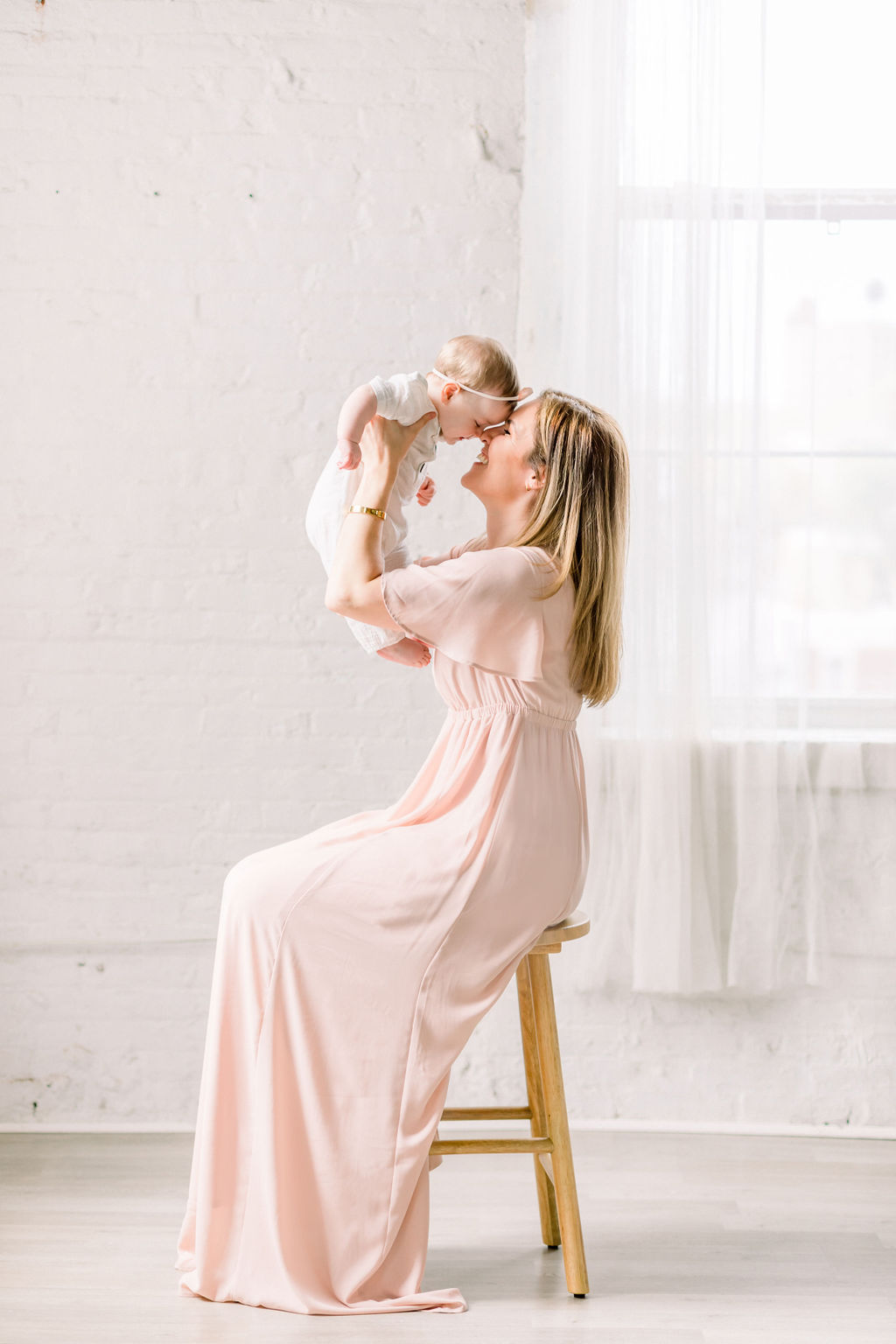 a mother wearing a pink dress and her daughter in a white romper during a studio motherhood session