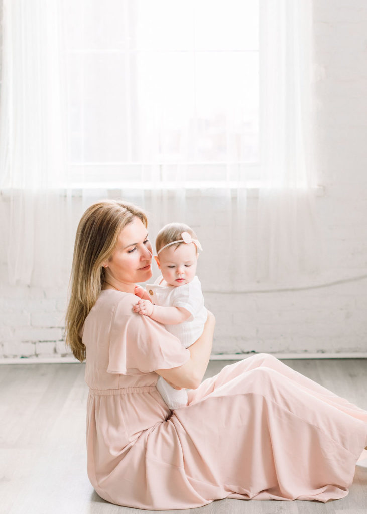 a mother wearing a pink dress and her daughter in a white romper during a studio motherhood session