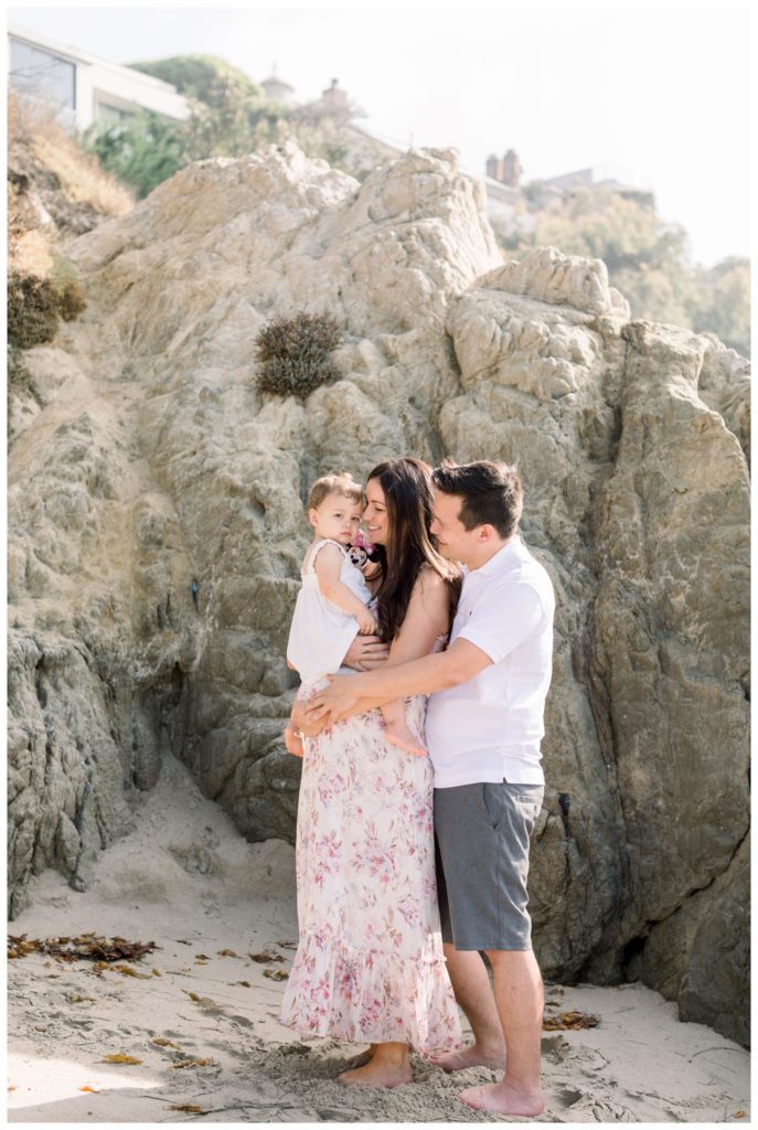 A family snuggling on the beach in front of a large rock formation - their selected location for family photos
