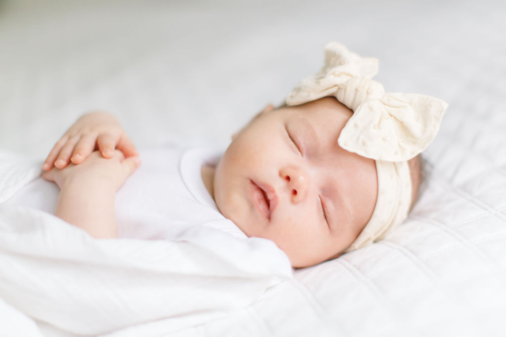 A newborn baby wearing a cream bow headband