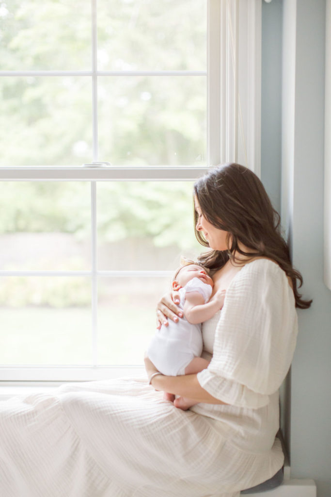 A mother and baby snuggle in a window seat during a Princeton NJ lifestyle newborn session