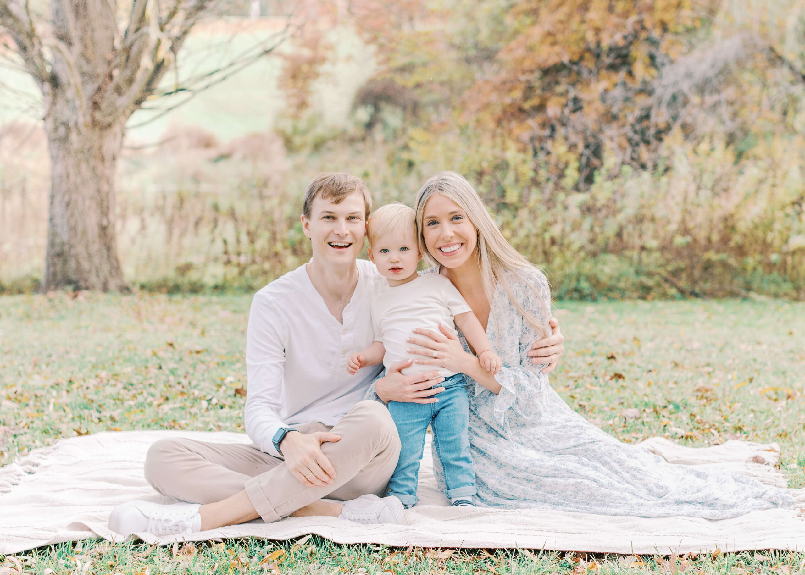 Image of Mom, Dad, and little boy sitting on a blanket at a park smiling and looking at the camera.