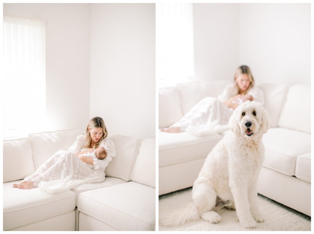 A mother and her newborn sit on a white couch during their in-home newborn session. Their goldendoodle sits in front of them.