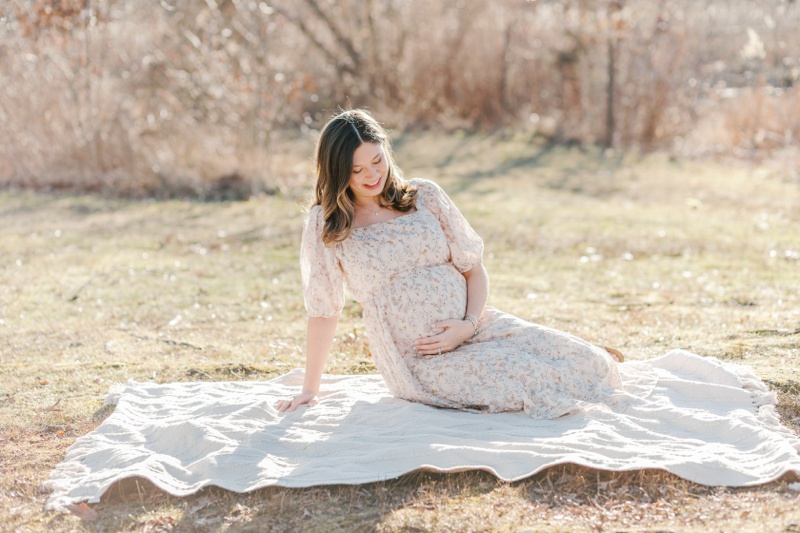 A pregnant woman sits on a blanket during maternity photos at Loantanka Brook Reservation