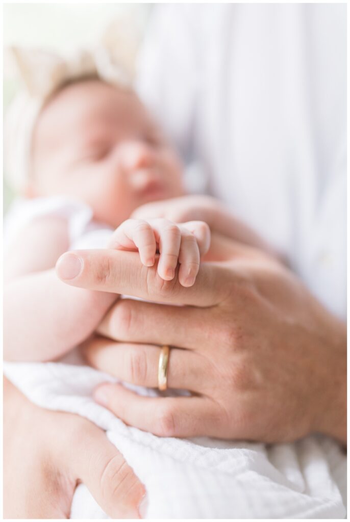 A newborn baby girl holds her father's finger during newborn photos at home. 