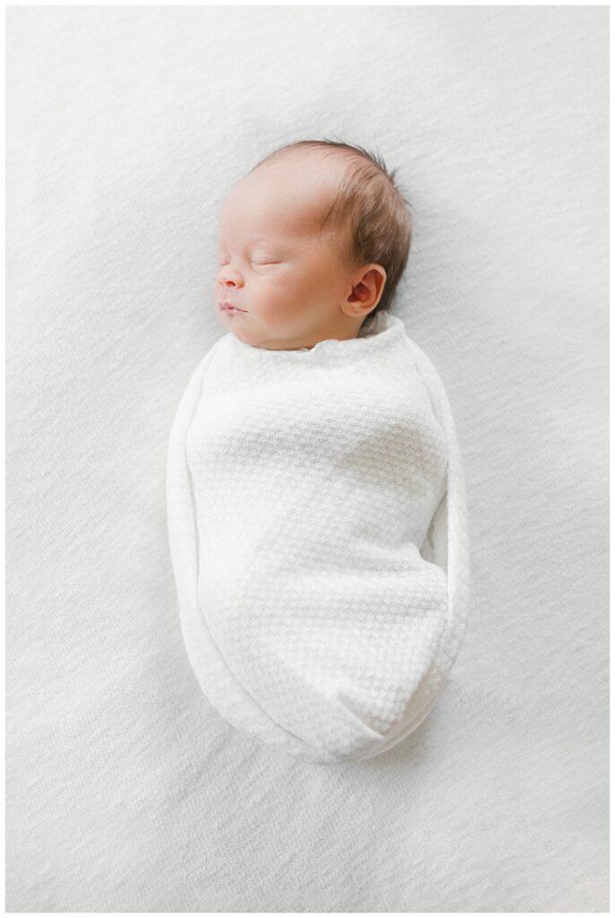 A newborn baby wrapped in a white swaddle during newborn photos at home