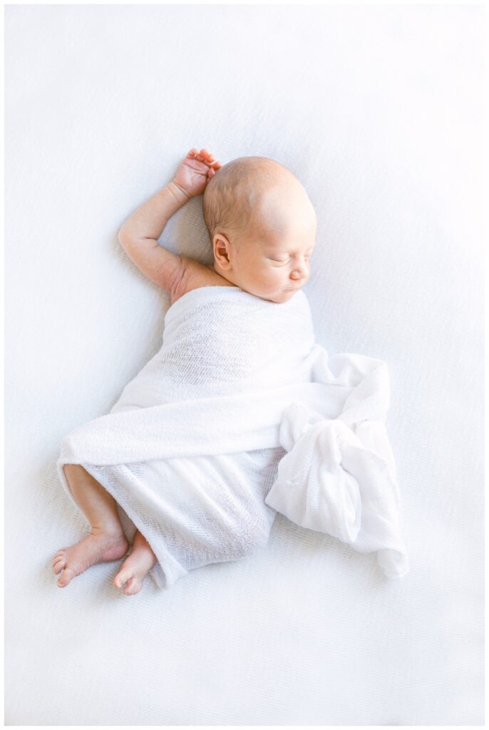 A newborn baby wrapped in a white swaddle during newborn photos at home. 