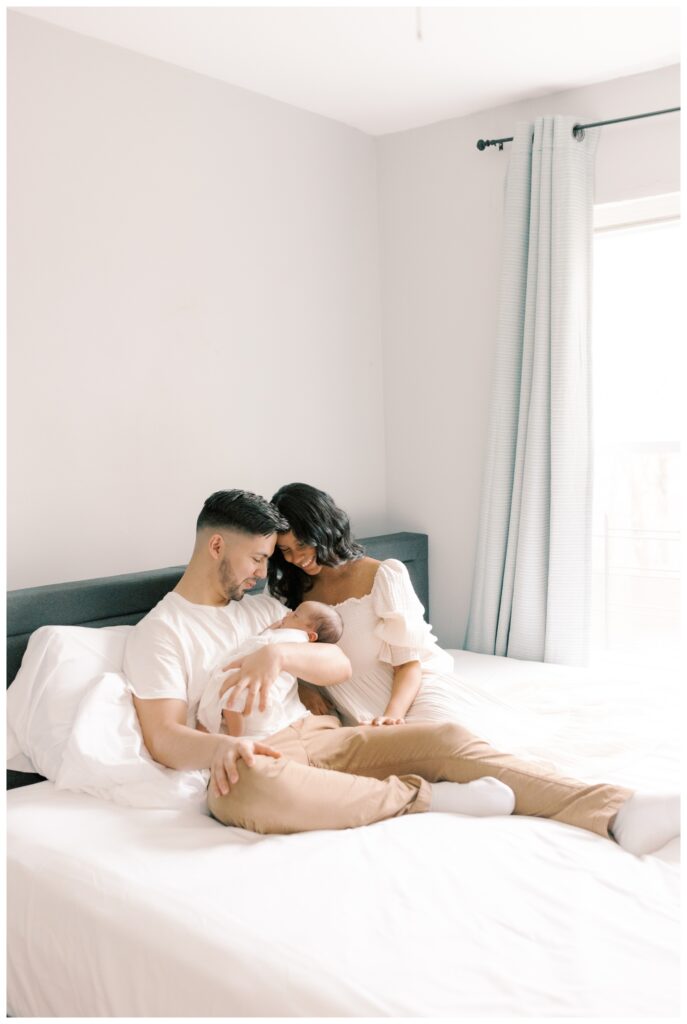 A couple sits on their bed holding their newborn during a lifestyle in-home newborn session
