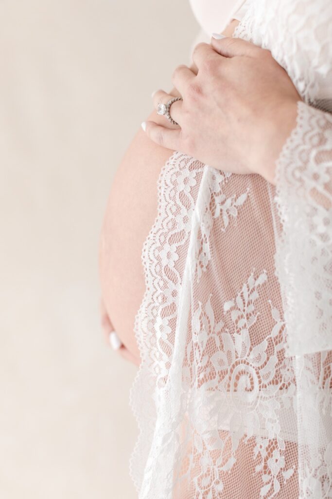 A pregnant woman wearing a whitelace robe cradles her stomach during her studio maternity photos after loss