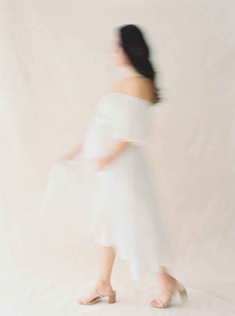 A pregnant woman wearing a white off the shoulder dress cradles her stomach during her studio maternity photos after loss