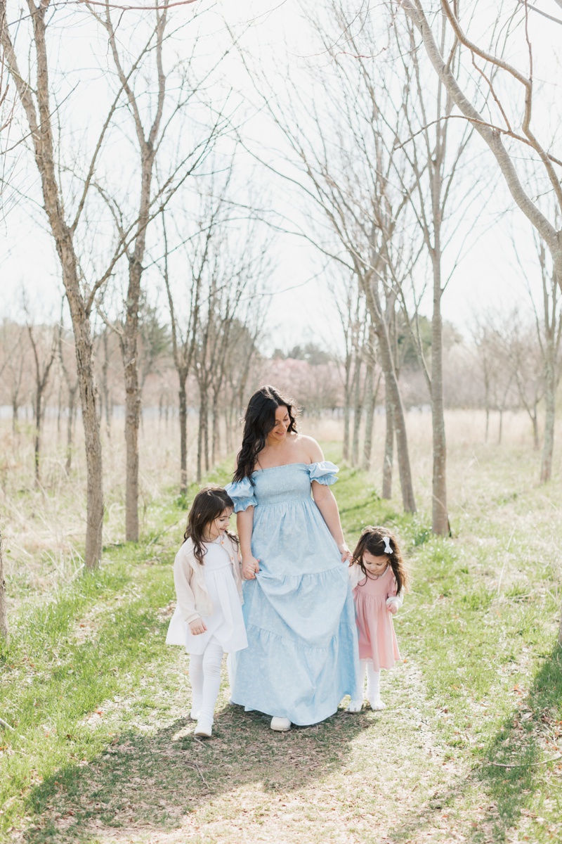 A woman wearing a blue dress holds her two daughters' hands as they walk together during a Mommy and Me Photo Session in New Jersey.