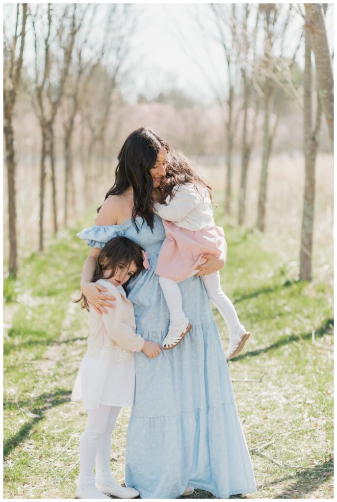 A mother snuggles with her two daughters during their motherhood portrait session. 