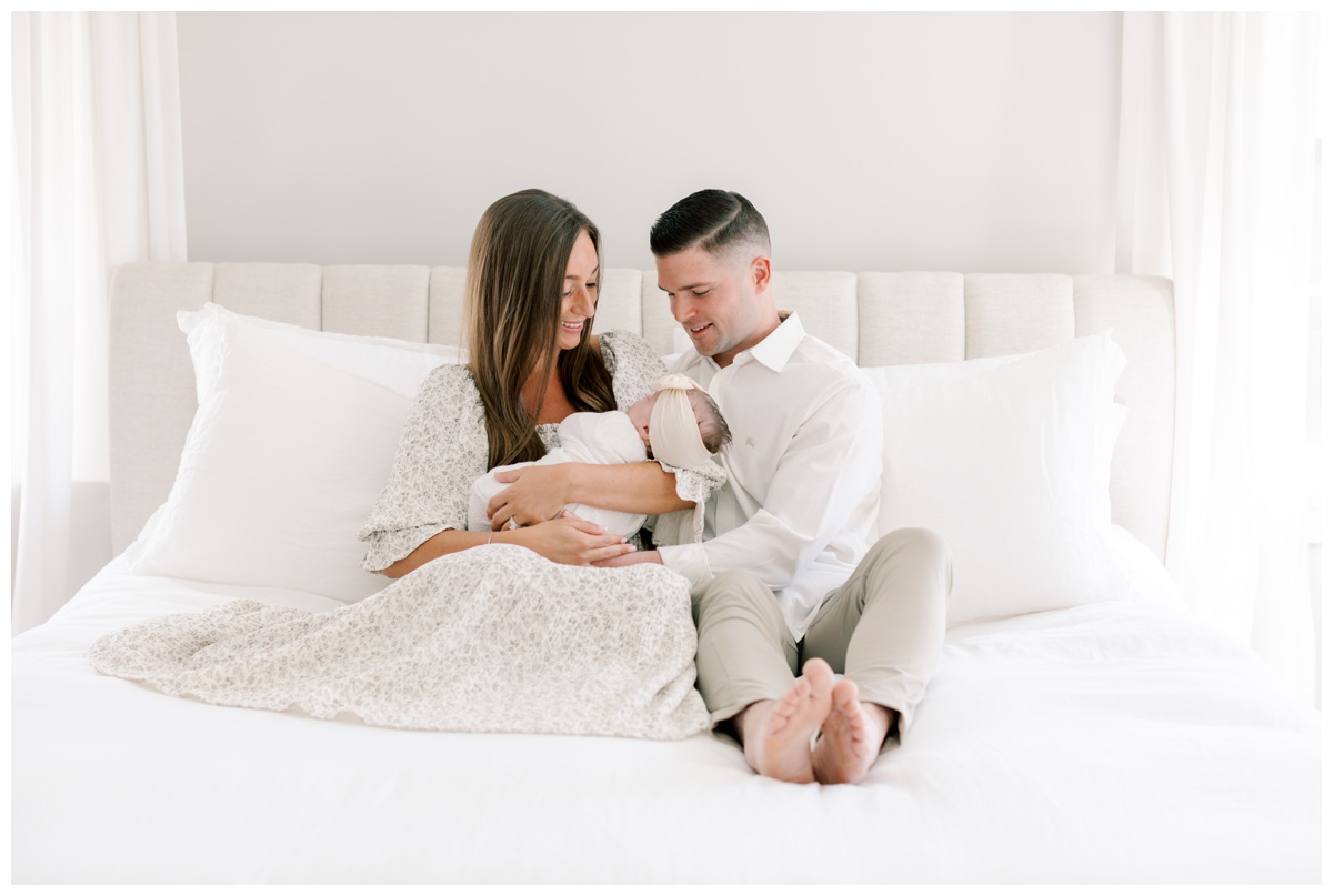 A couple sits on the bed gazing down at their newborn during their cranbury nj newborn photography session photographed by Kate Voda Photography