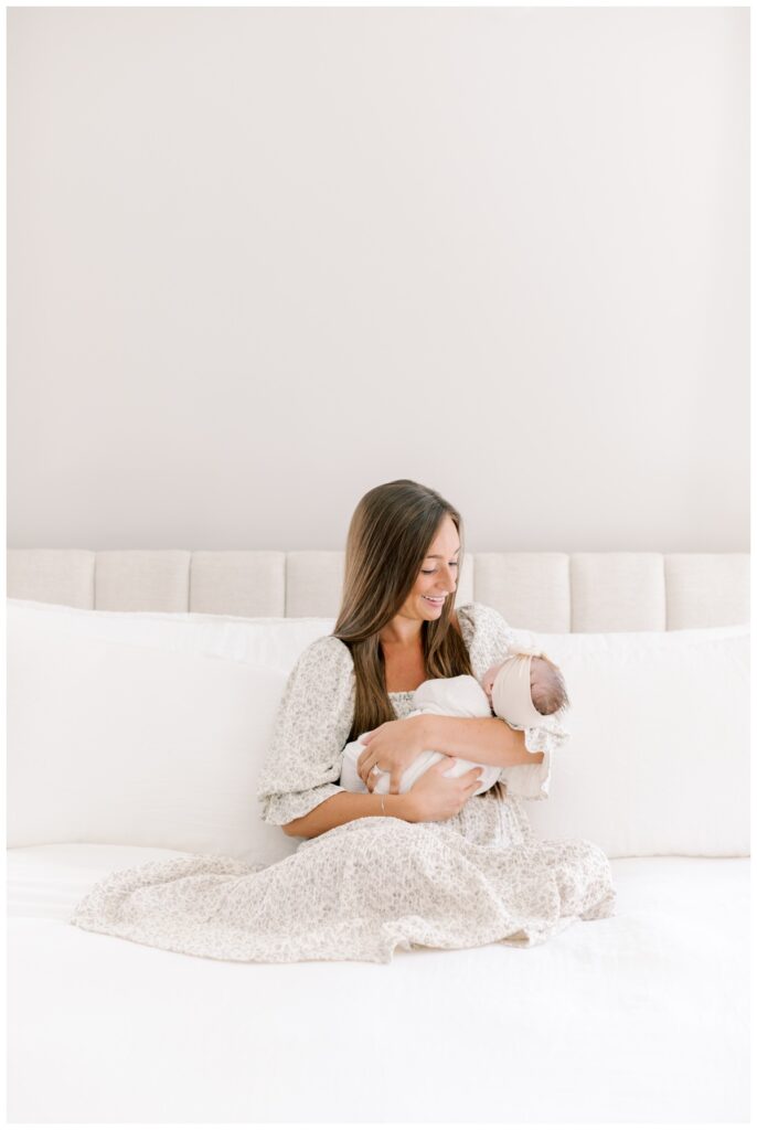 A woman sits on her bed and holds her newborn baby girl