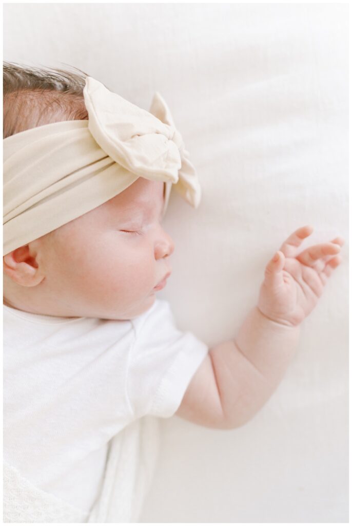 A newborn baby girl in a white onesie sleeps during her Cranbury NJ Newborn Photography Session photographed by Kate Voda Photography