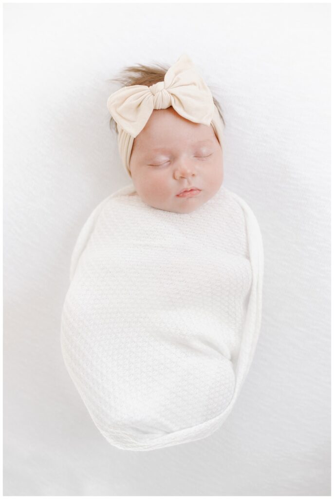 A newborn baby girl sleeps while wrapped in a white swaddle, photographed by Kate Voda Photography