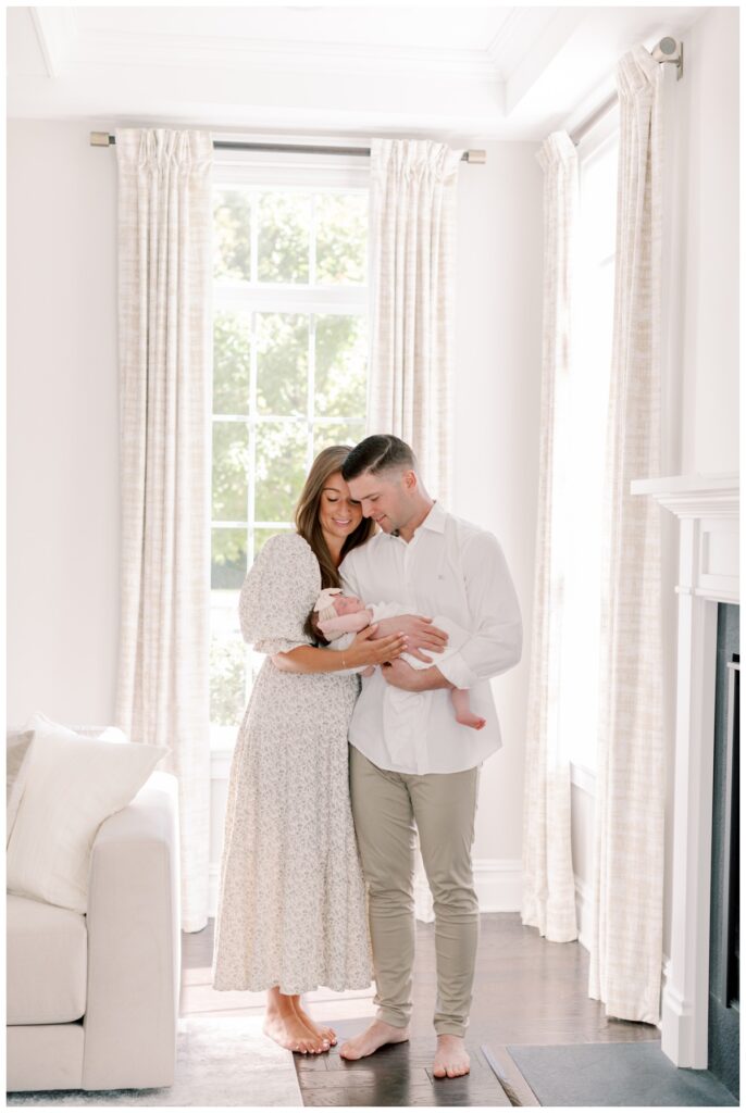 A couple holds their sleeping baby in their sun-drenched living room during their newborn photos photographed by Kate Voda Photography