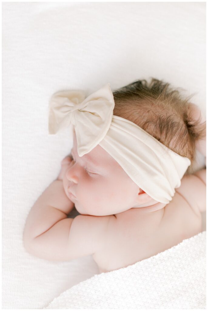 A baby sleeps comfortable during her Cranbury NJ newborn photography session photographed by Kate Voda. She is sleeping on a white backdrop.