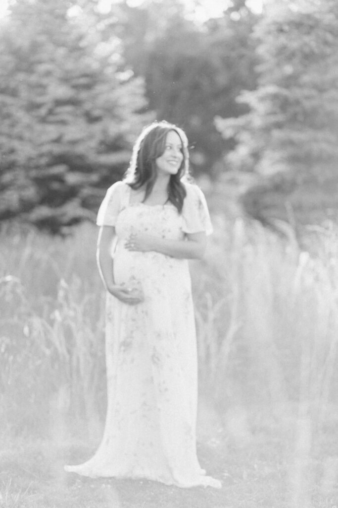 A pregnant woman stands outside during her NJ maternity photo session cradling ehr belly.