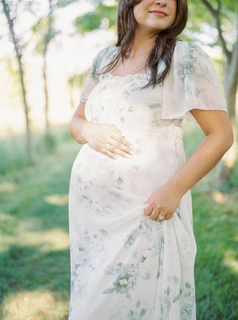 A close up image of a woman's pregnant belly in the sun. She is wearing a floral dress.