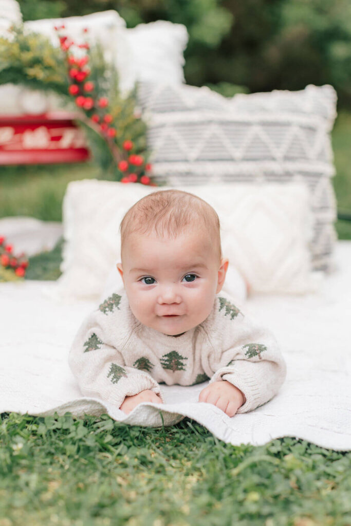 Mini Session, Half, or Full: Which Is Right for Your Family? (2026) Baby in a Christmas tree sweater doing tummy time on a cream blanket, with pillows and red berries behind, in Cranbury, NJ