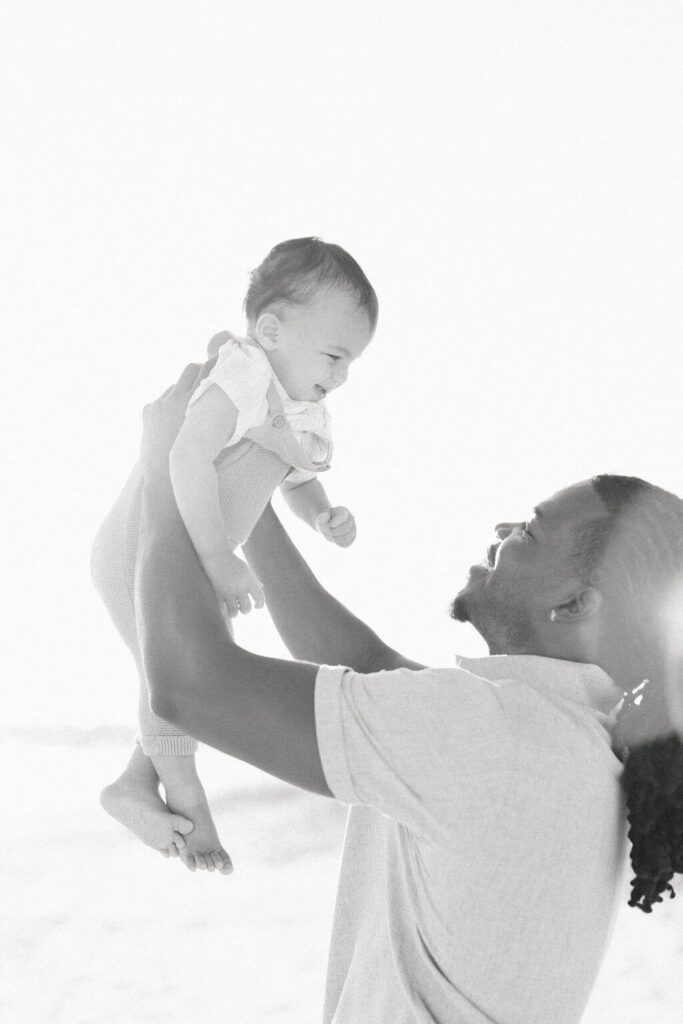 Mini Session, Half, or Full: Which Is Right for Your Family? (2026) black and white dad lifting toddler beach nj