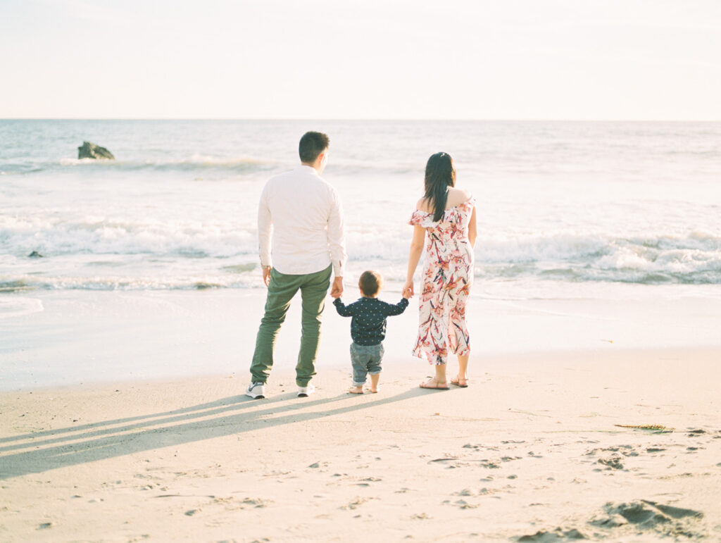 A family stands together looking at at the water during their family photos at the beach.