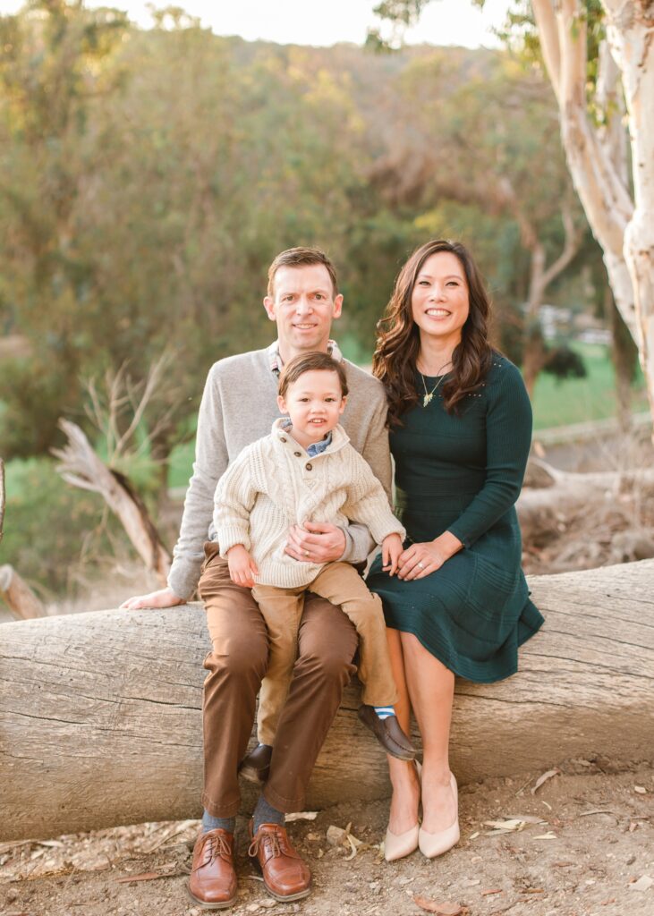 A family of 3 sits together on a log during family photos