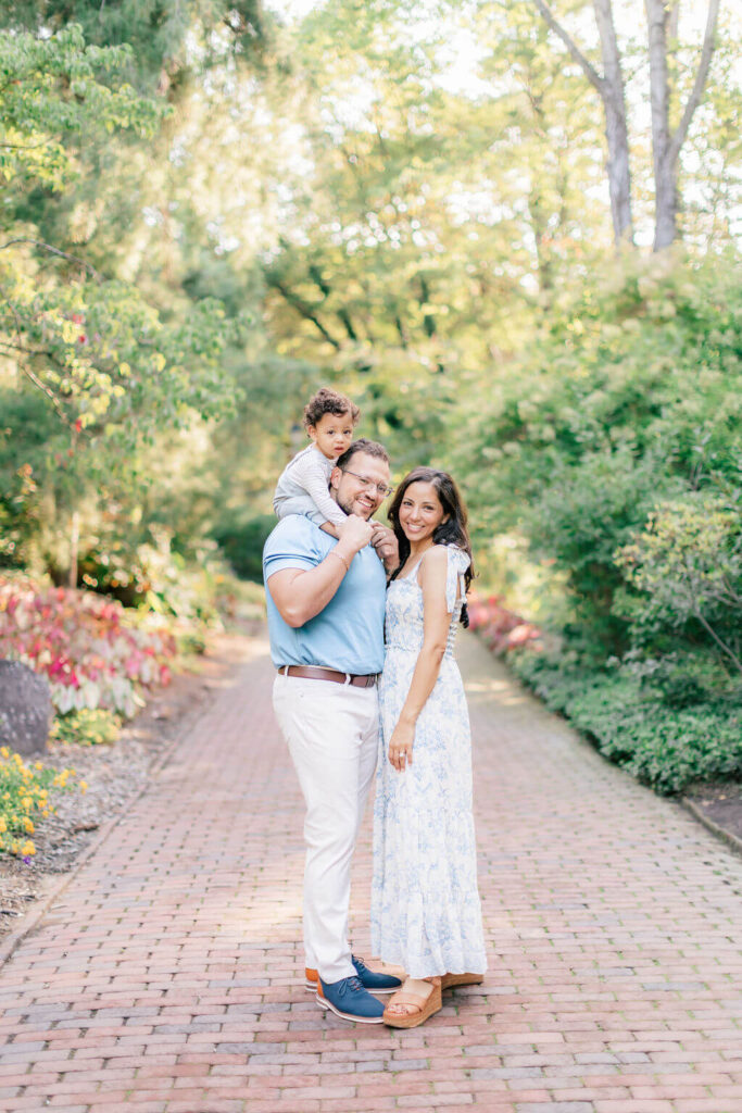 Mini Session, Half, or Full: Which Is Right for Your Family? (2026) Smiling family portrait on a garden path at Sayen House and Gardens in Central New Jersey, with the toddler sitting on dad's shoulders