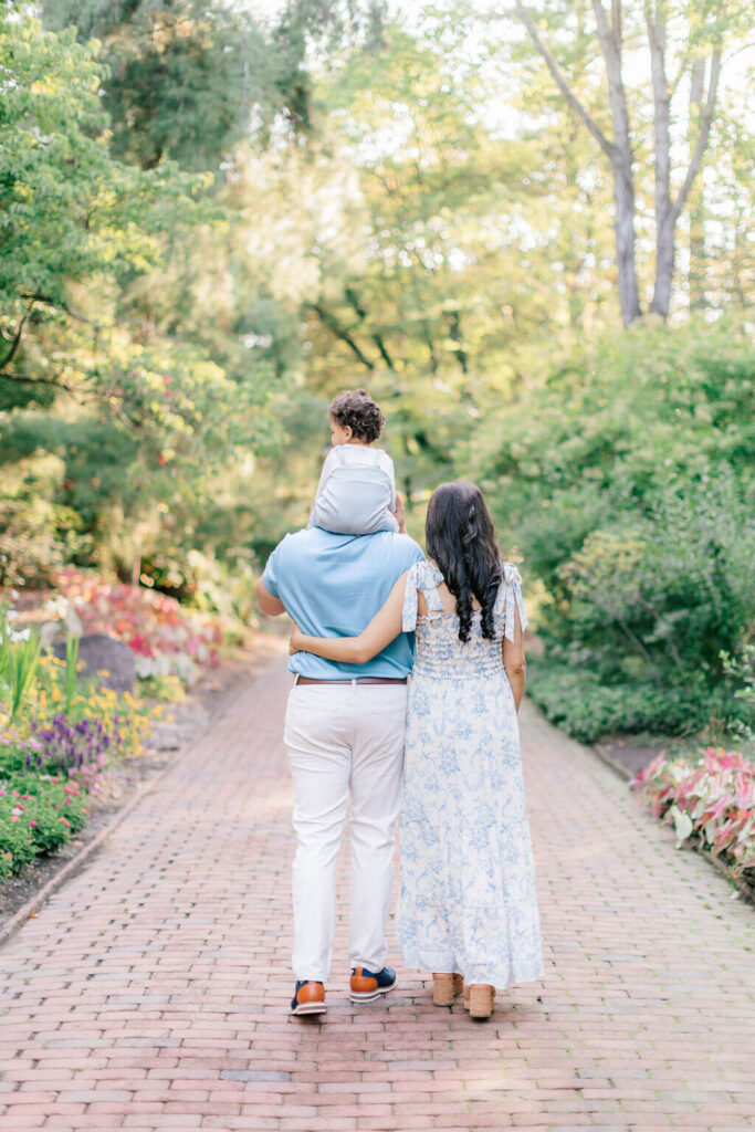 Mini Session, Half, or Full: Which Is Right for Your Family? (2026) Family walking away down a flower lined brick path at Sayen House and Gardens, with their toddler riding on dad's shoulders