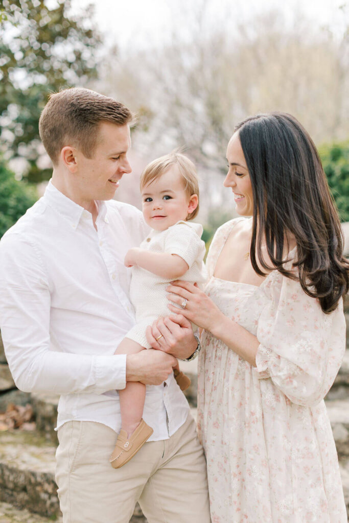 Mini Session, Half, or Full: Which Is Right for Your Family? (2026) Mom and dad smiling at their one year old son in a cream knit romper during a spring family session at Cross Estate Gardens in New Jersey