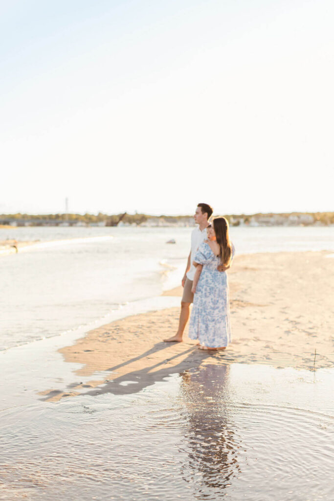 Mini Session, Half, or Full: Which Is Right for Your Family? (2026) Mom and dad standing together at the water's edge at Fisherman's Cove in Manasquan, NJ, with their toddler in mom's arms and their reflection in the tide pool