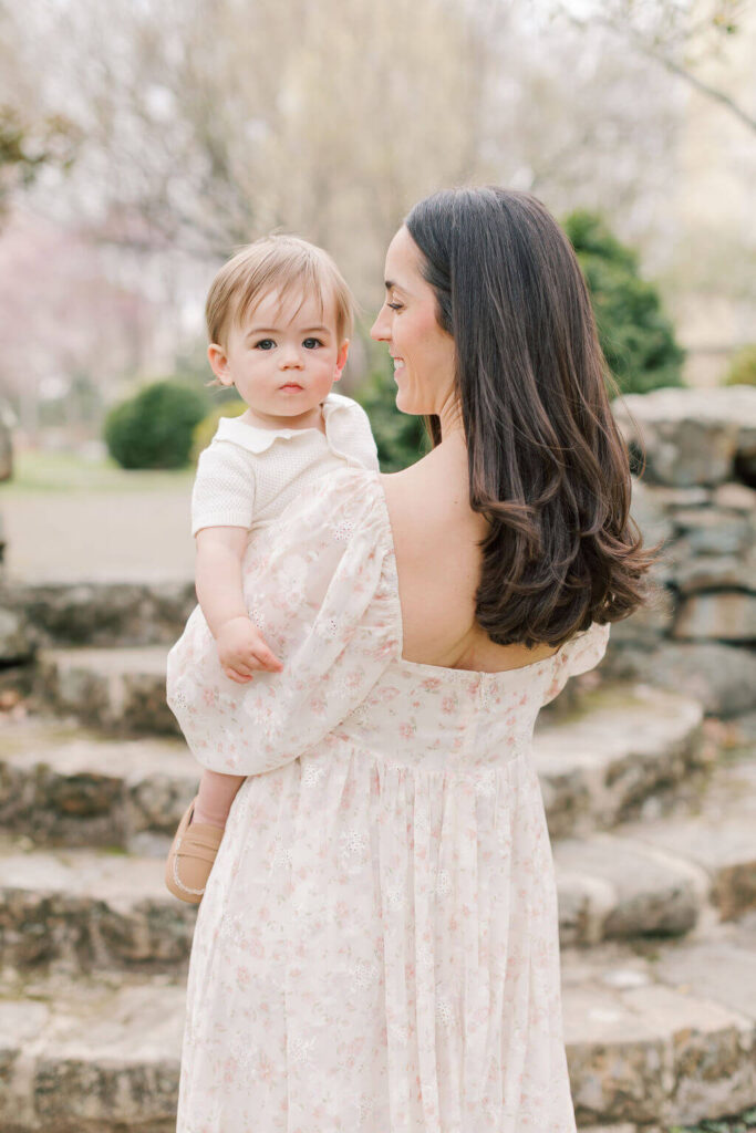 Mini Session, Half, or Full: Which Is Right for Your Family? (2026) Mom in a floral dress holding her one year old son on her hip beside stone steps and spring blossoms in New Jersey
