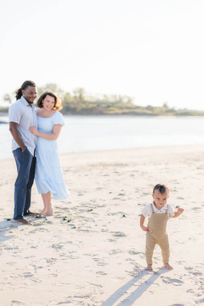 Mini Session, Half, or Full: Which Is Right for Your Family? (2026) Toddler standing on his own in the sand while mom and dad smile at him by the water during a family session at the Jersey Shore