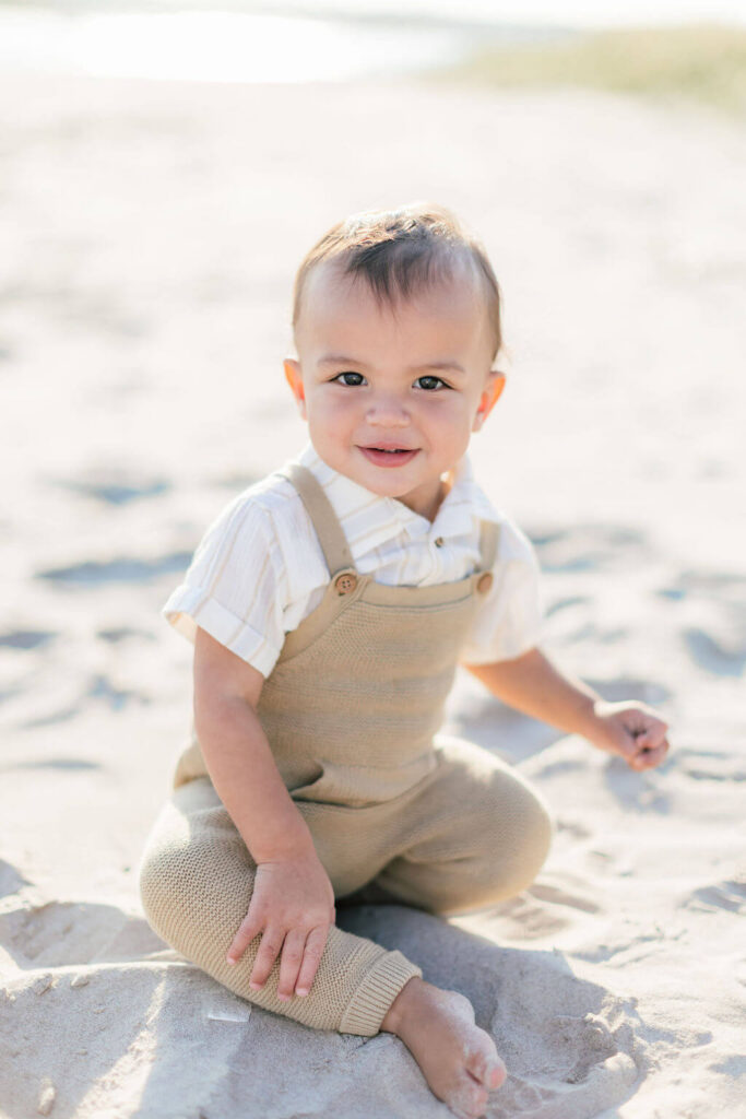 Mini Session, Half, or Full: Which Is Right for Your Family? (2026) Smiling toddler in knit overalls sitting in the sand at Fisherman's Cove in Manasquan, NJ