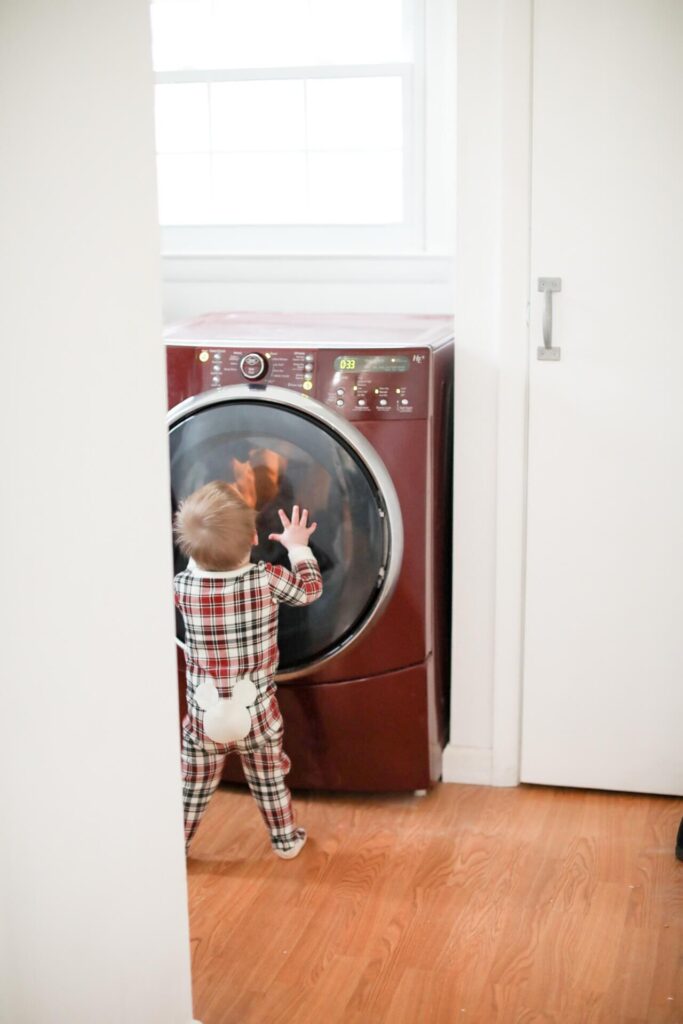 A toddler stands in front of a washing machine