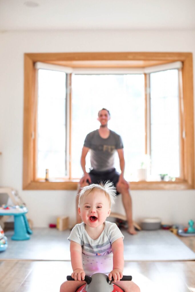 Toddler on a red ride on toy smiles during pictures of everyday life
