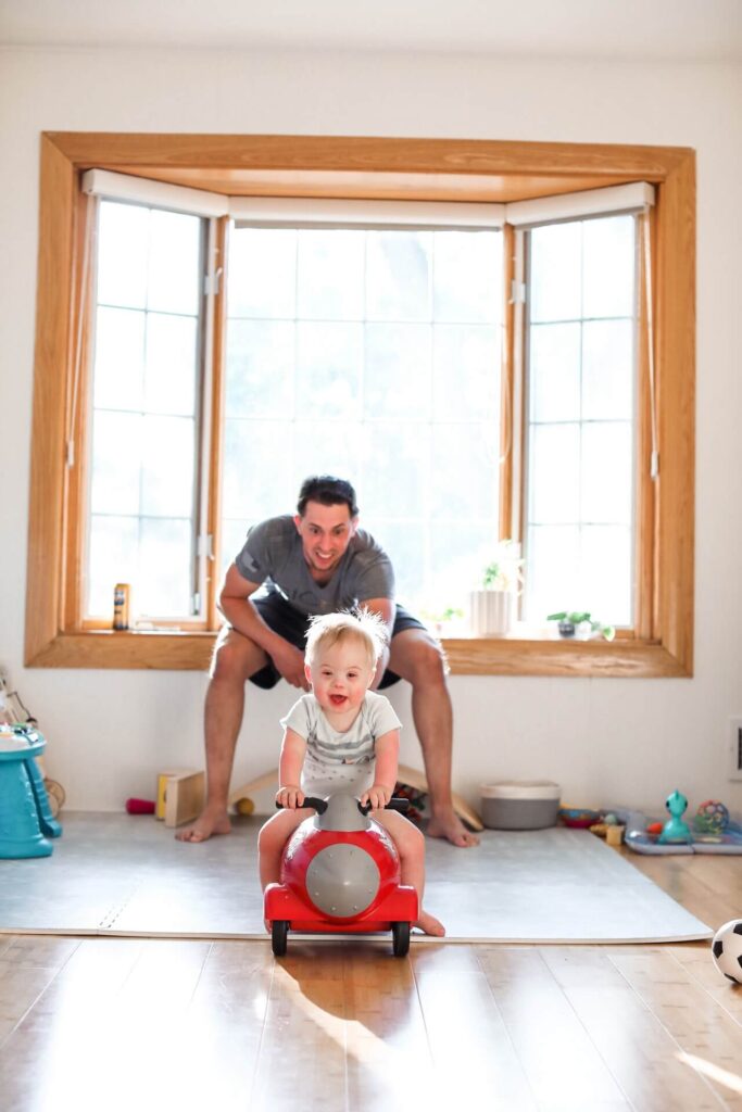 Toddler on a red ride on toy smiles during pictures of everyday life