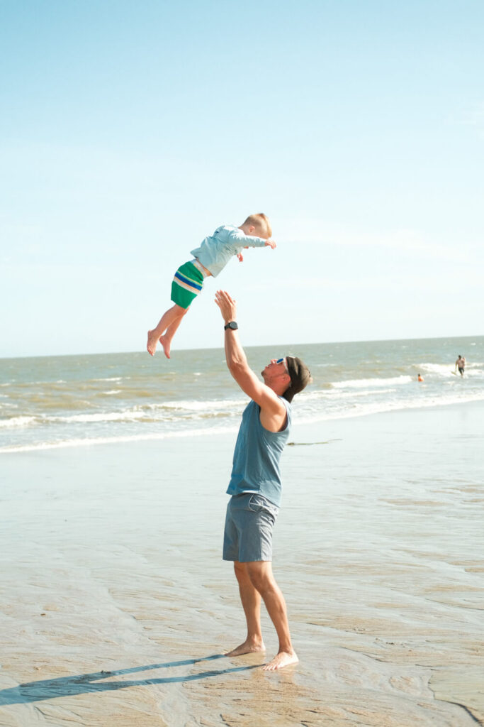 Father tossing young child in the air on a New Jersey beach on a sunny day