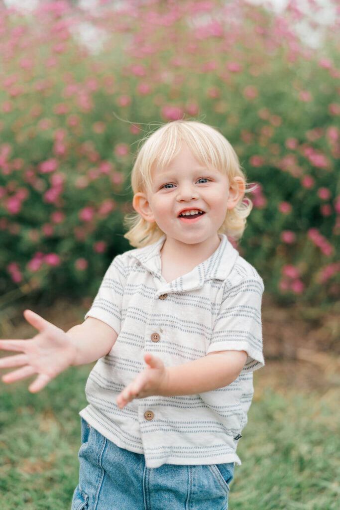 Beautiful Flower Farm Family Photos | Pretty Bird Farm, NJ Toddler boy laughing and reaching toward the camera in front of pink flowers at Pretty Bird Farm in NJ