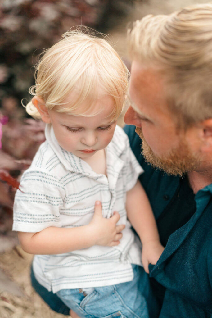 Beautiful Flower Farm Family Photos | Pretty Bird Farm, NJ Dad holding his toddler son close as the little boy looks down at something in his hands