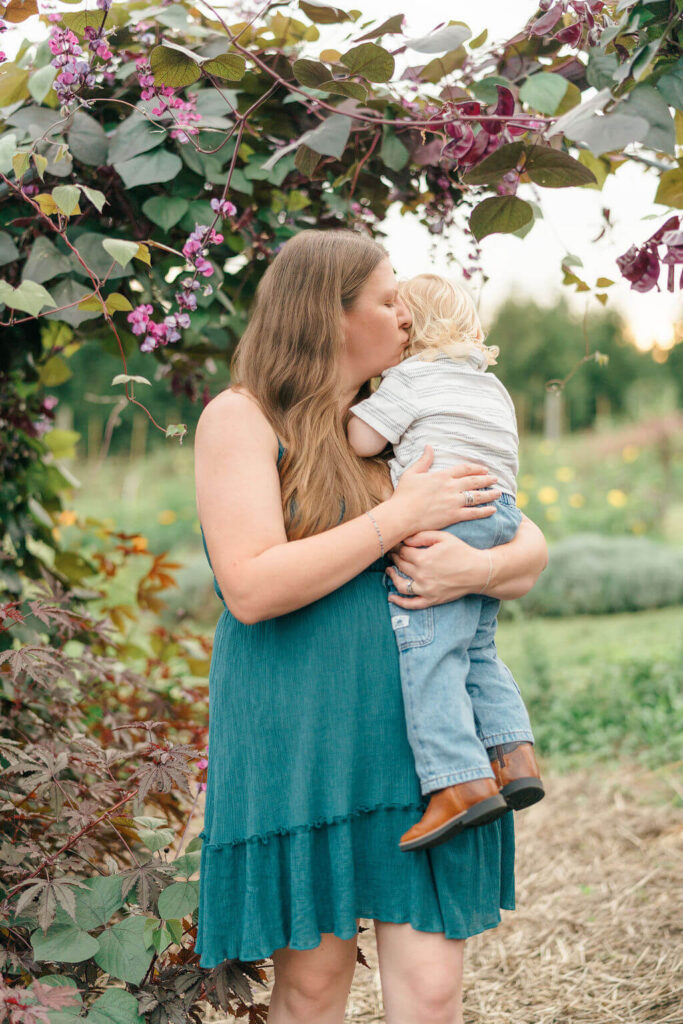 Beautiful Flower Farm Family Photos | Pretty Bird Farm, NJ Mom kissing her toddler son under an arbor of hyacinth bean vines at Pretty Bird Farm in NJ
